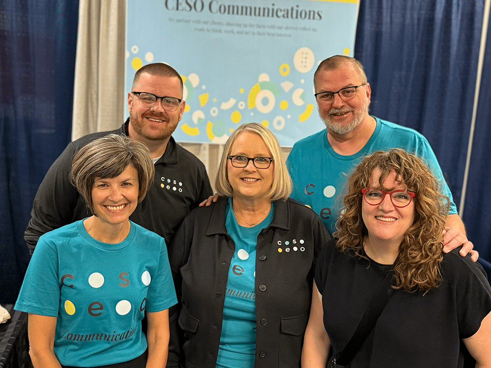 Five CESO Communications team members huddled together smiling